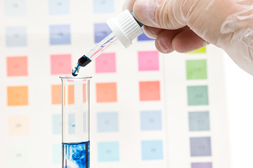 Hand dripping pH indicator into test tube with visible color change in test fluid